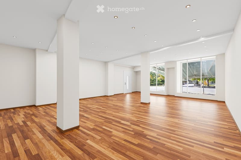 Empty room with polished wooden flooring, white walls, and recessed ceiling lighting. Large windows provide natural light and a view of the outdoors.