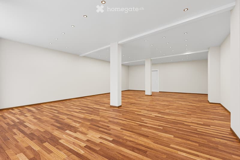 Empty room with wooden flooring and white walls, featuring recessed ceiling lights and white columns.