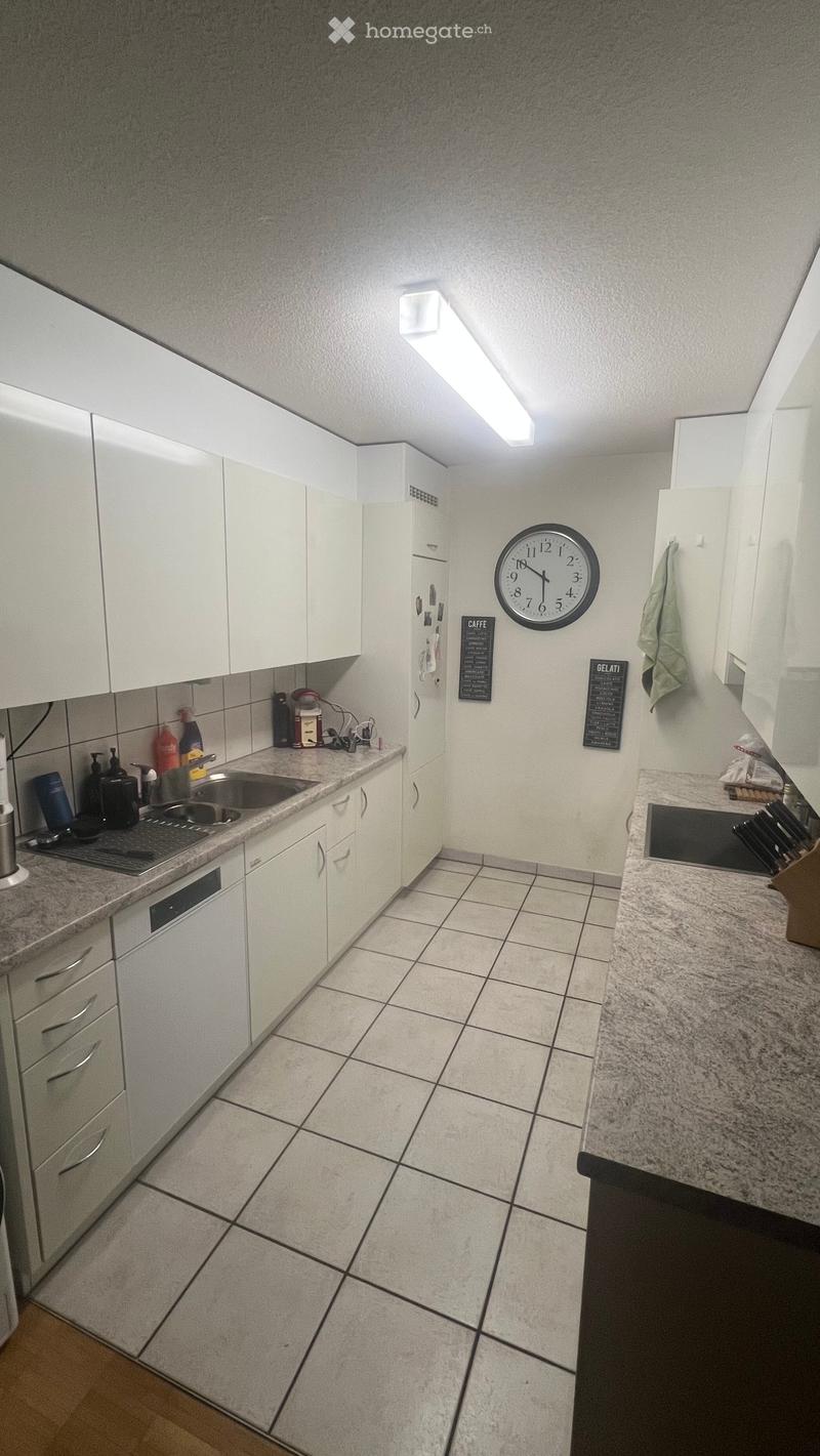 Modern kitchen with white cabinets, granite countertops, tiled floor, and stainless steel appliances including a sink, oven, and refrigerator. A clock is mounted on the wall, and a knife block is visible on the counter.
