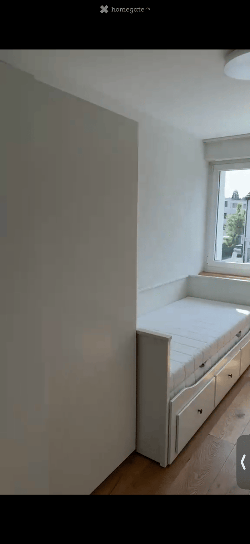 A small, modern living space with a built-in sofa and a cabinet, featuring wooden flooring and white walls.