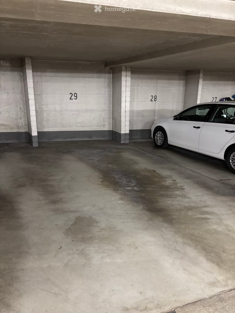 Underground parking space with a single white car parked in bay number 27, marked bays27, 28, and 29 visible on the walls.