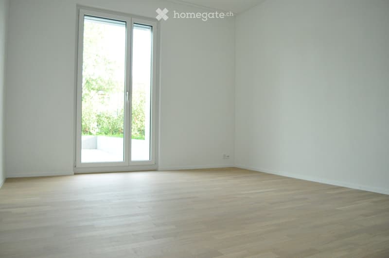 Empty room with light wooden flooring and white walls, featuring a large sliding glass door that opens to a balcony or outdoor area.