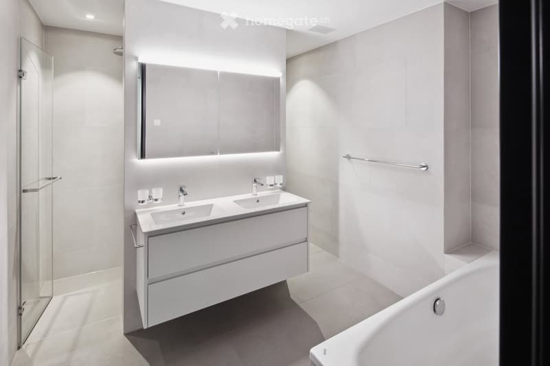 Modern bathroom with a double sink vanity, large mirror with integrated lighting, bathtub, and glass shower enclosure.