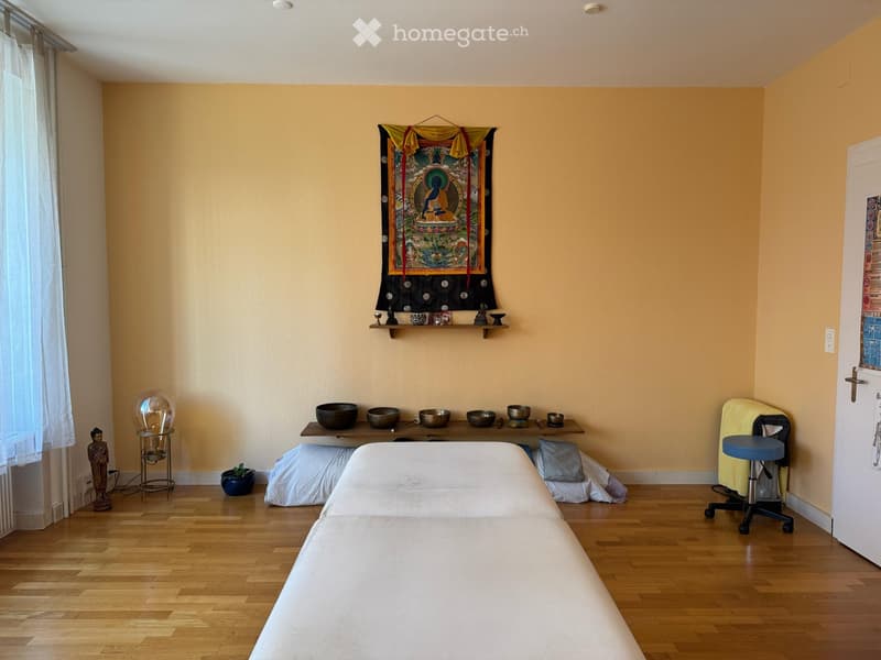 massage table, wooden floor, beige walls, table with bowls, decoration on wall, curtains
