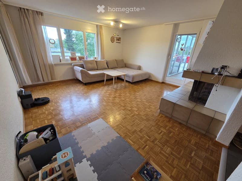 Living room with wooden flooring, large windows, a sofa, coffee table, fireplace, and various toys and decorations.