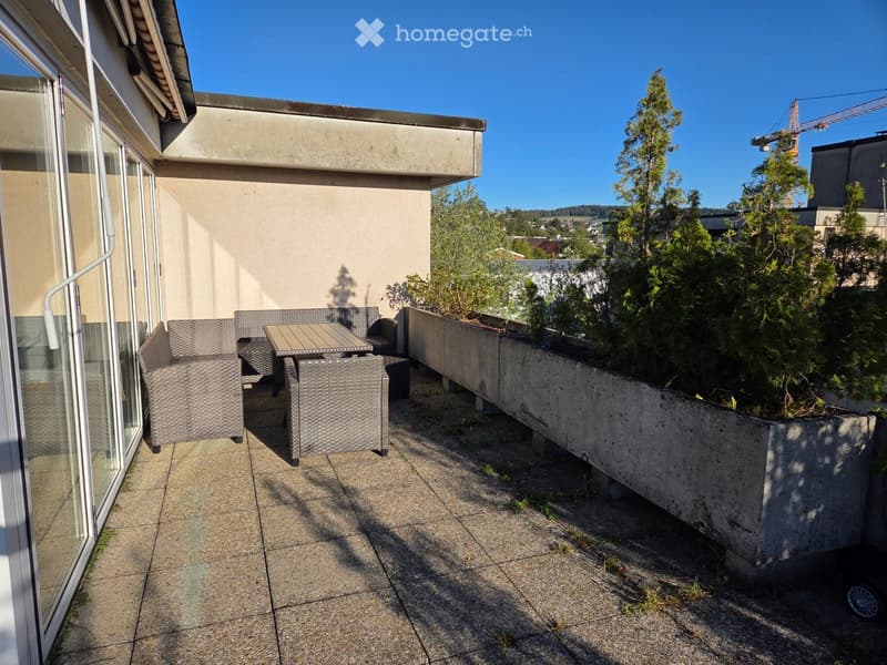 Balcony with a sofa, table, and greenery in the background.