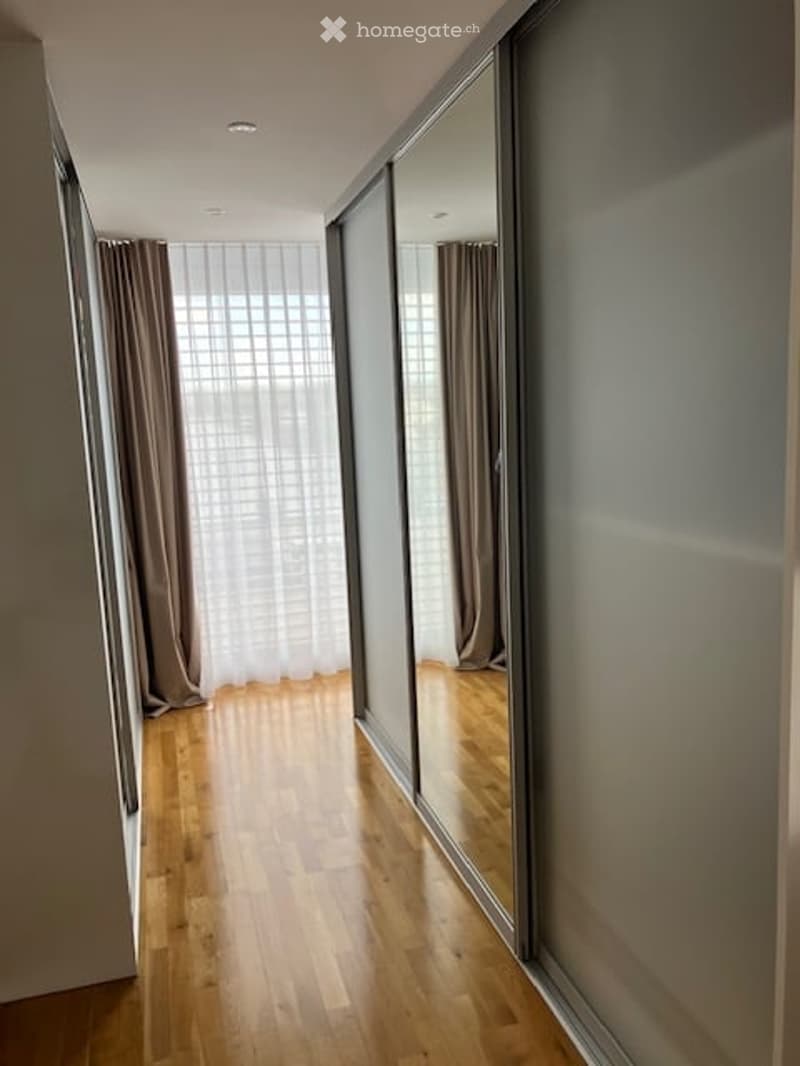 A modern hallway with wooden flooring, large mirrored closet doors, and sheer curtains allowing natural light to filter in.