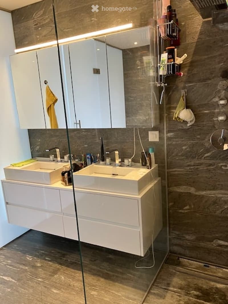 Modern bathroom with double sink vanity, large mirror, and glass-enclosed shower area.
