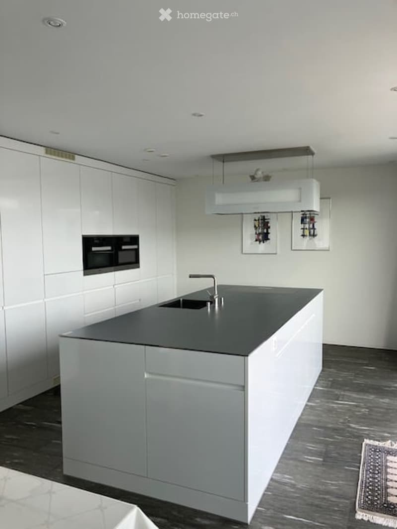 Modern kitchen with white cabinets, a central island, and a black countertop. Features a built-in oven, a sink with a modern faucet, and framed pictures on the wall.