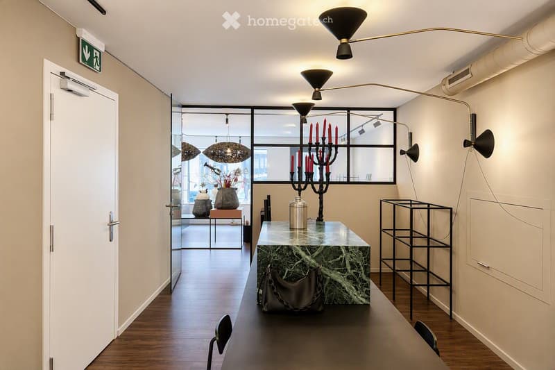 Modern hallway with wooden flooring, large windows, and contemporary decor including a marble table, candle holder, and sleek lighting fixtures.