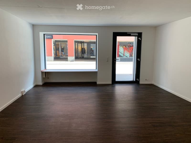 Empty room with wooden flooring, white walls, large window, and a glass door leading outside.