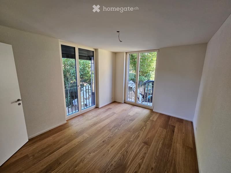 Empty room with wooden flooring, white walls, and large sliding glass doors leading to a balcony.