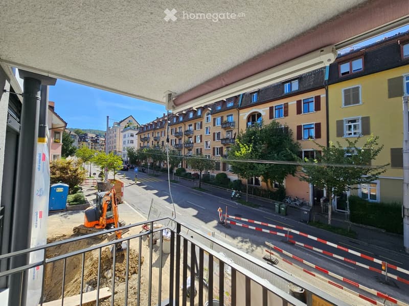 Balcony overlooking a street with buildings, trees, and construction activity.