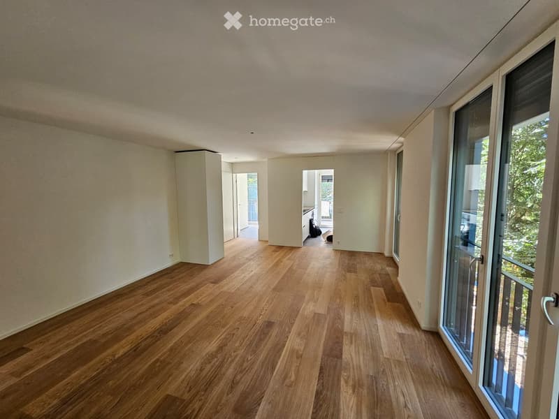 Empty room with wooden flooring, white walls, and large glass sliding doors leading to a balcony.