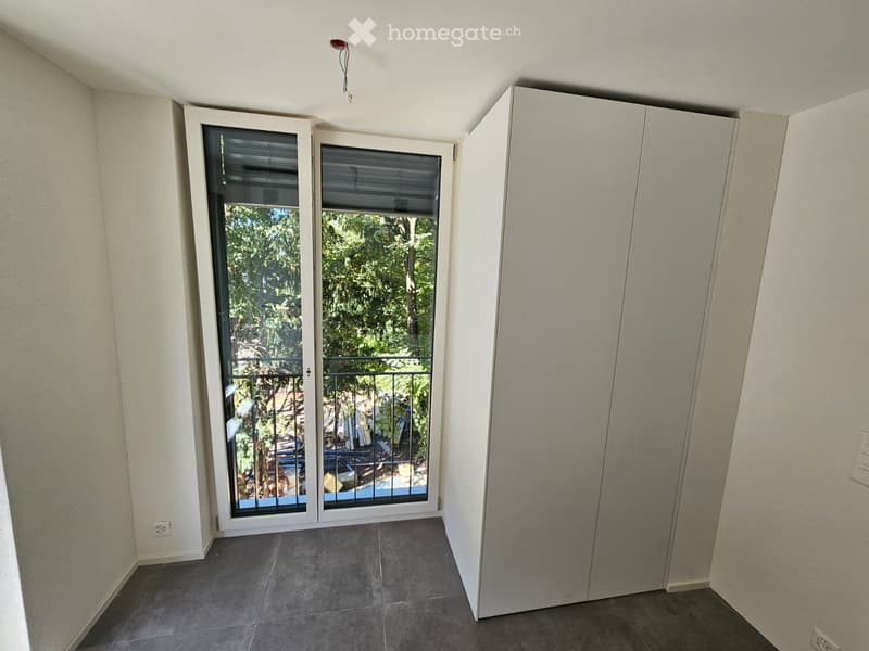 Empty room with tiled floor, white walls, and a large sliding glass door leading to a balcony with a metal railing and outdoor view.