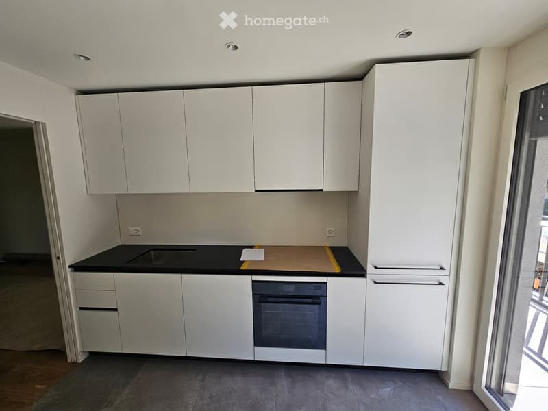 Modern kitchen with white cabinets, black countertop, and built-in oven. The space is clean and organized, with a window providing natural light.