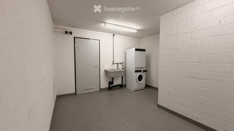 A small utility room with a washing machine, sink, and tiled floor.