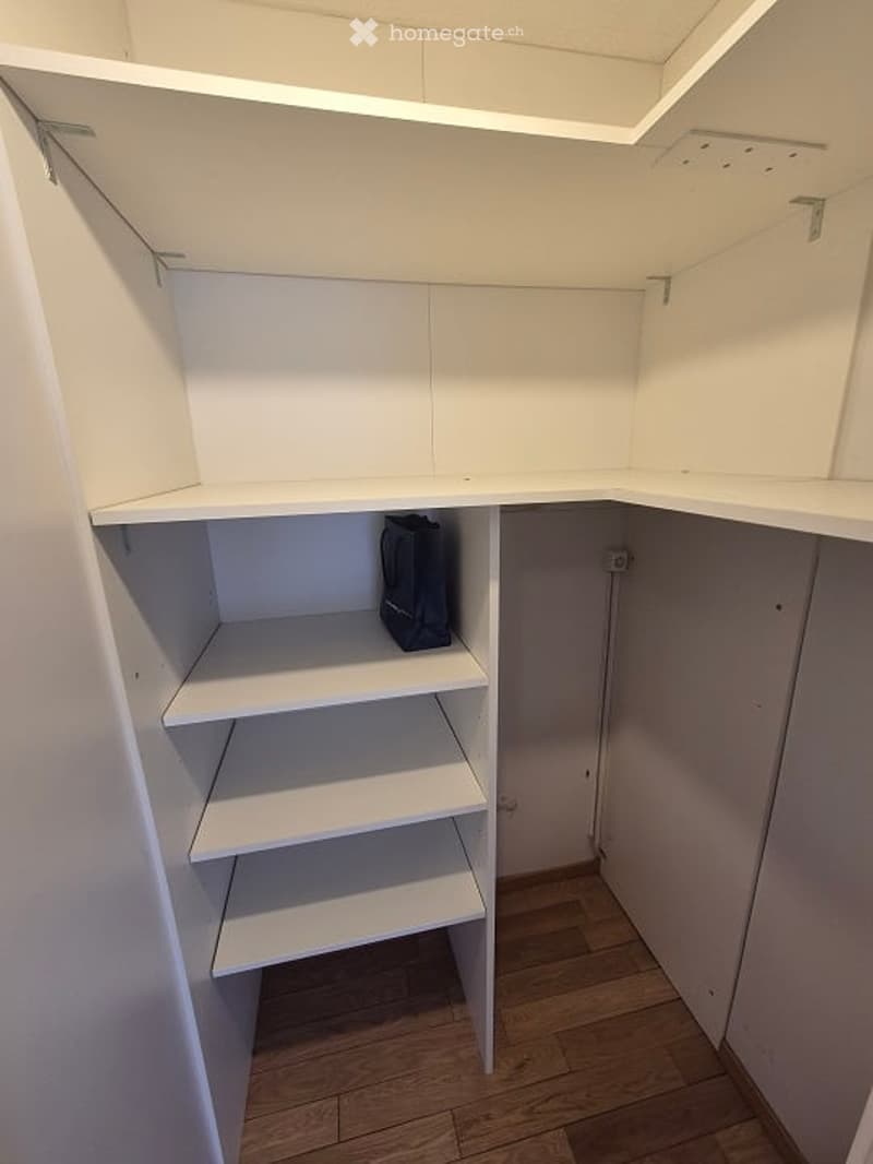 Empty closet with white built-in shelving units and wooden flooring.