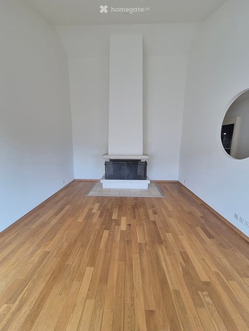 Completely empty room with wooden flooring and a fireplace in the center.