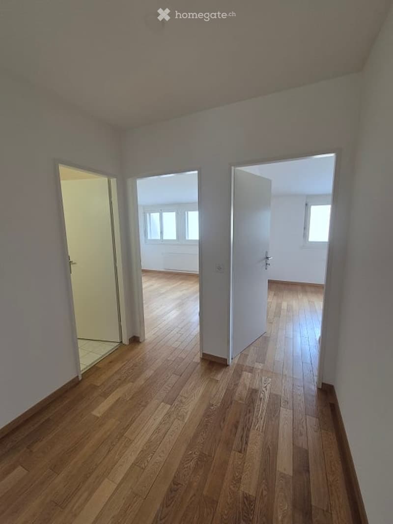 Empty hallway with wooden flooring, white walls, and open doors leading to adjacent rooms.