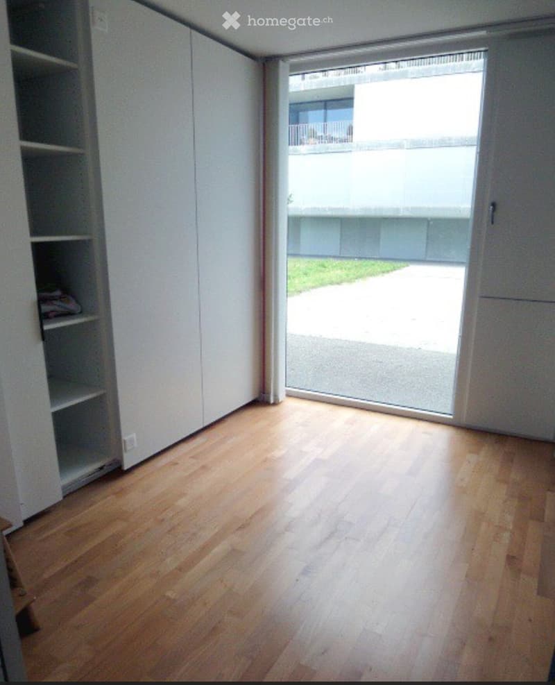 Empty room with wooden flooring, white walls, and a large sliding glass door leading to an outdoor area.