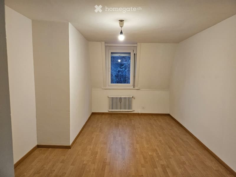 Empty room with wooden flooring, white walls, a single window, a radiator, and a ceiling light fixture.