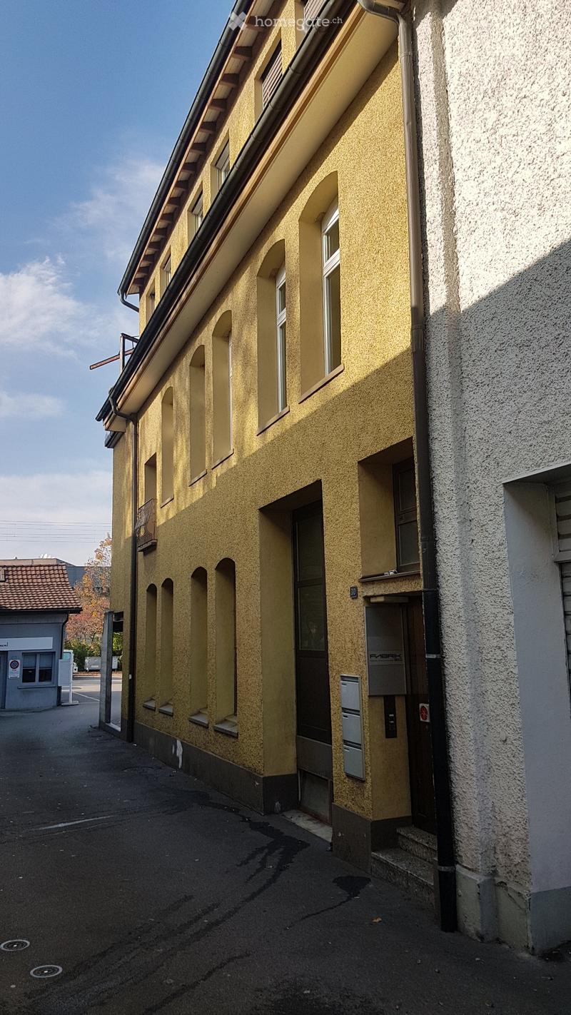 Four-story building with yellow facade, arched windows, and a balcony on the second floor.
