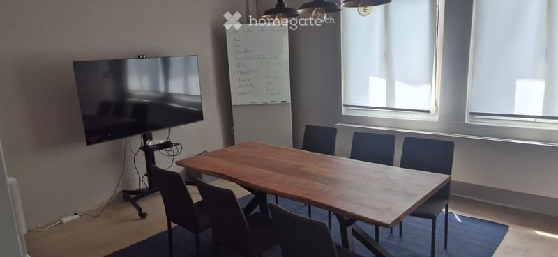 Meeting room with a large wooden table, several chairs, a large screen, and a whiteboard with handwritten notes.