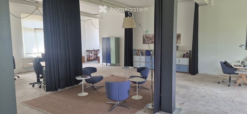 Modern, open-plan room with blue chairs, white tables, a floor lamp, and shelves with books and decorative items.