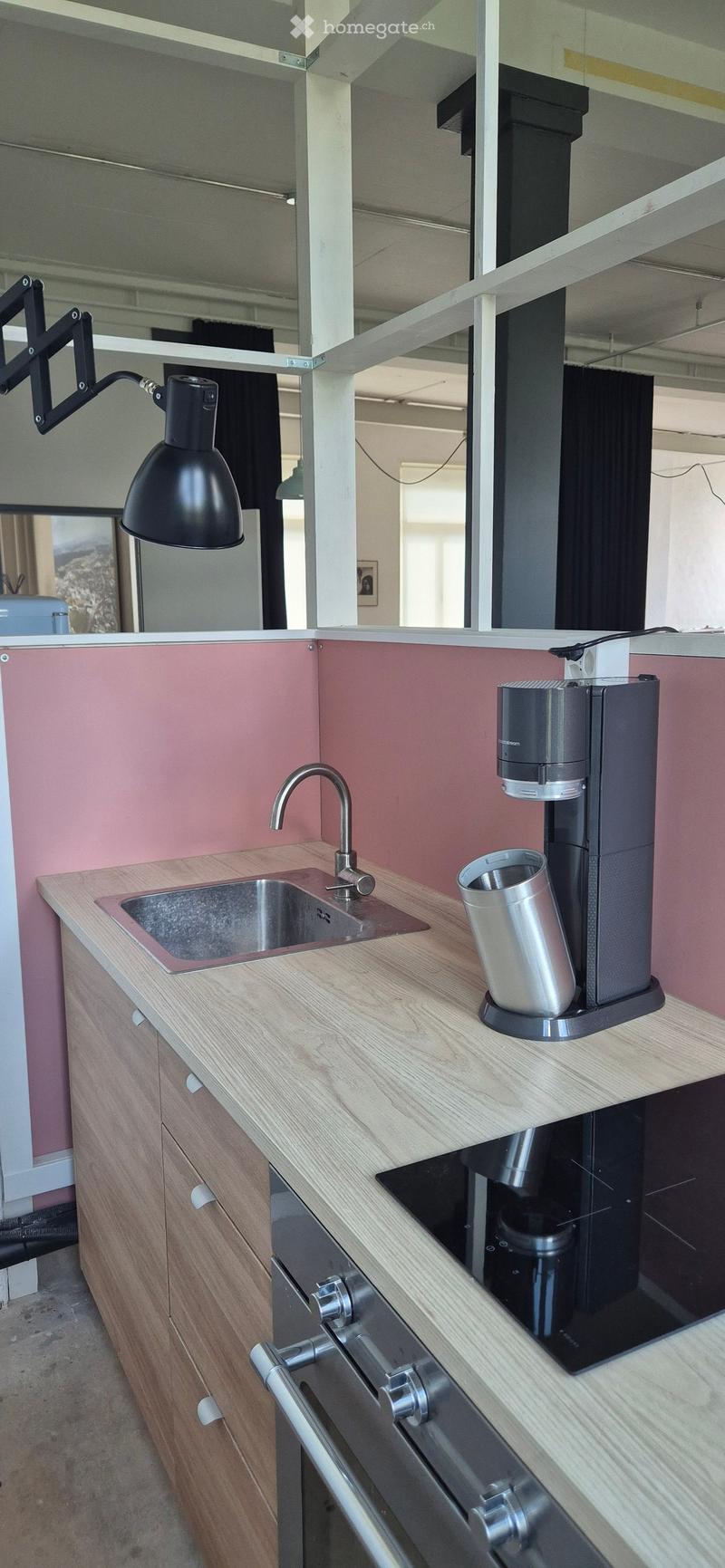 Modern kitchen with light wooden cabinets, stainless steel sink, faucet, and a black coffee machine with a cup on the counter.