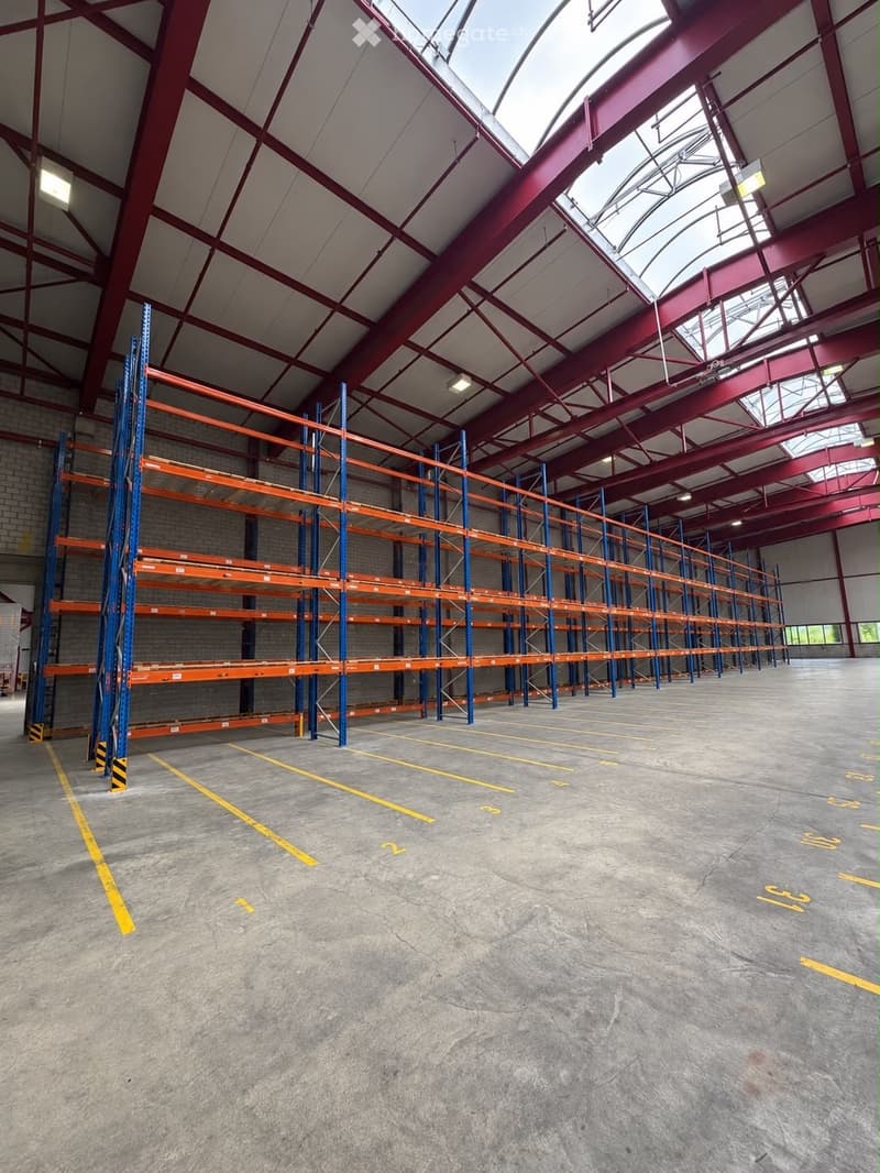 Large industrial warehouse with high ceilings, metal shelving units, and concrete floor marked with yellow lines.