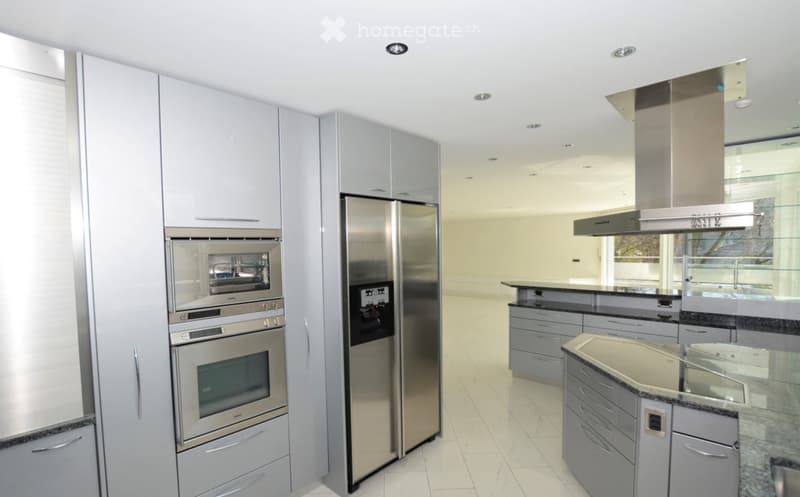 Modern kitchen with stainless steel appliances, including a refrigerator, oven, and kitchen island, complemented by grey cabinets and a sleek design.