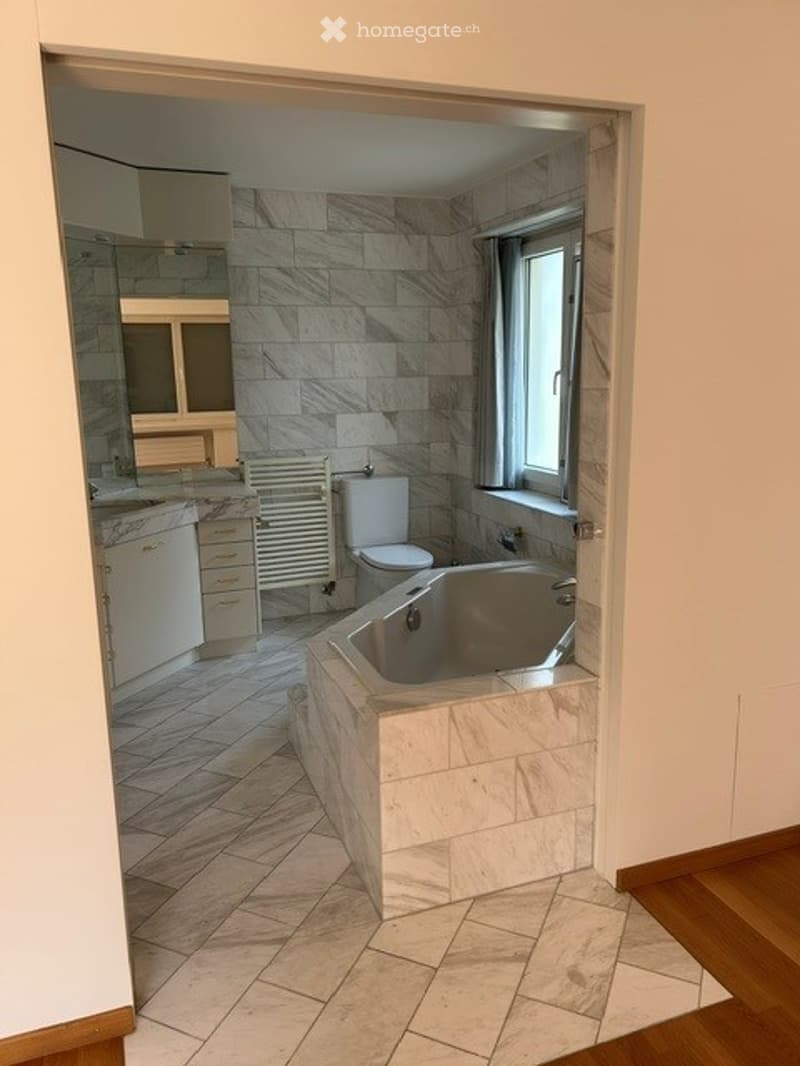Modern bathroom with marble tiles, a large bathtub, toilet, radiator, and a sink with cabinets.