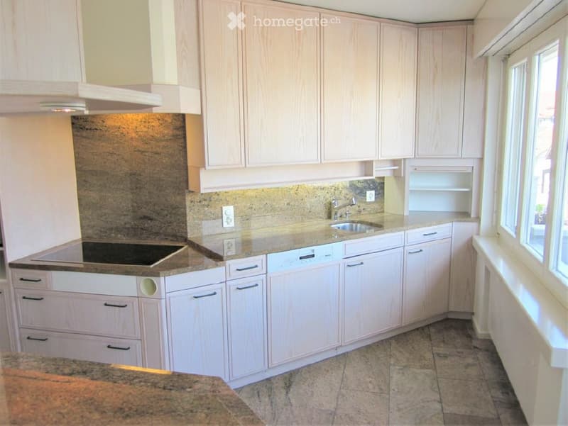 Bright kitchen with light wood cabinets, granite countertops, and stainless steel appliances including a sink, faucet, and dishwasher. Electric stove is visible on the left side.