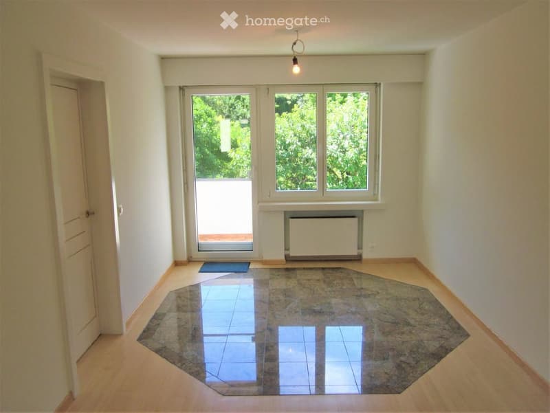 Empty room with wooden flooring, large windows, and a door leading outside. No furniture or equipment present.