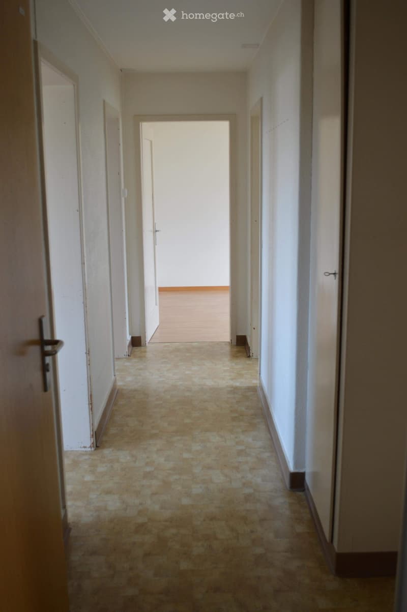 Empty hallway with tiled floor, white walls, and multiple doors leading to rooms.