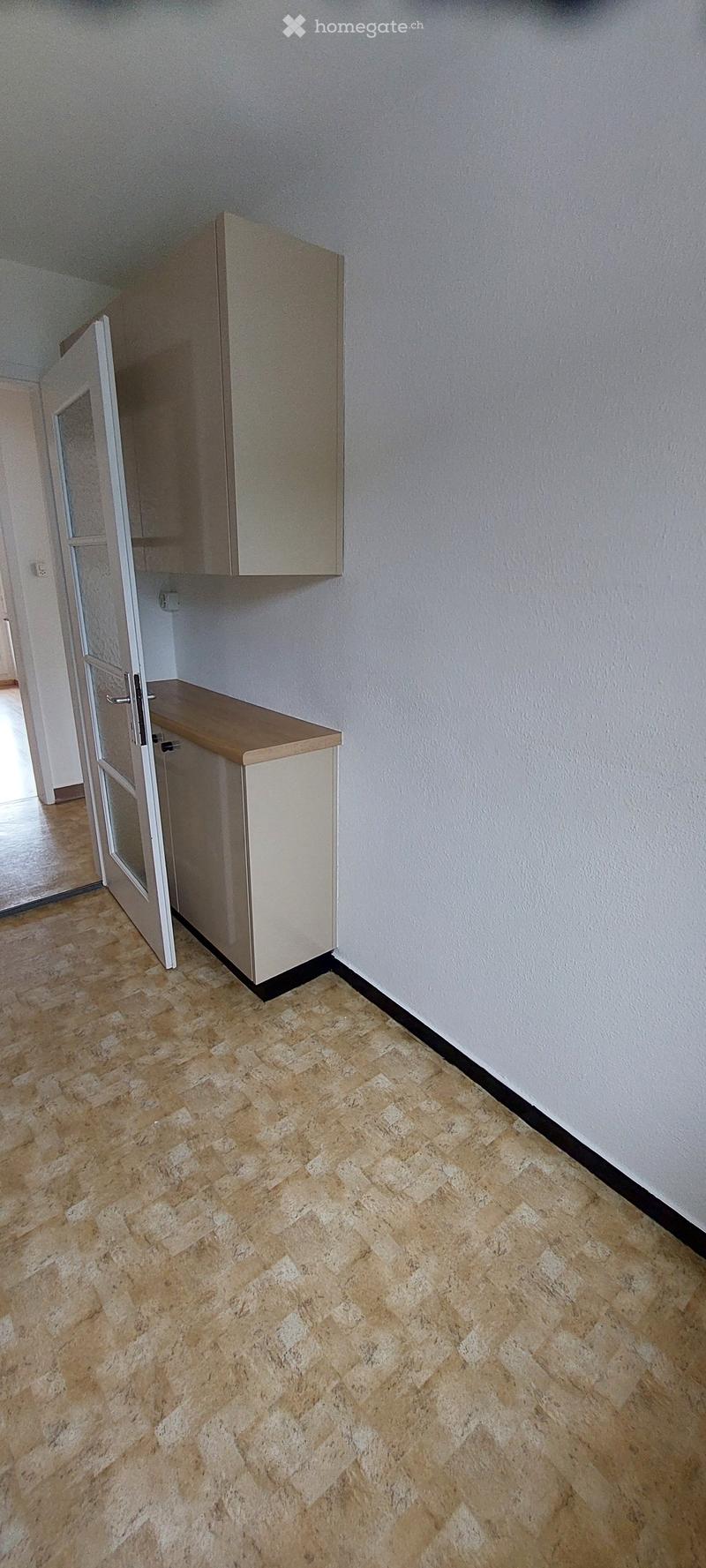 Empty hallway with light-colored walls, tiled floor, and built-in storage units on one side.