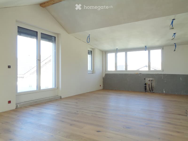 Empty room with wooden flooring, white walls, large windows, and exposed wooden beams on the ceiling.