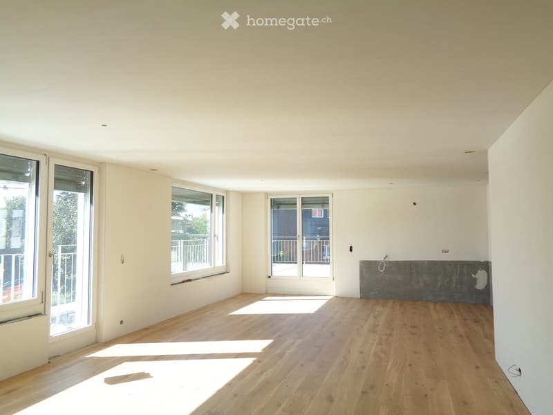 Empty room with wooden flooring, white walls, and large windows with sliding doors leading to a balcony.
