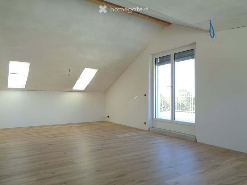 Empty room with wooden flooring, white walls, and large windows, featuring exposed wooden beams on the ceiling.