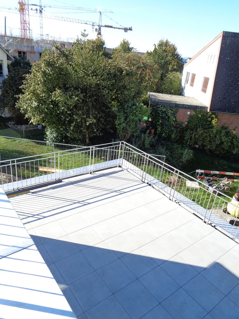 Roof terrace with tiled flooring, metal safety railing, and surrounding greenery.