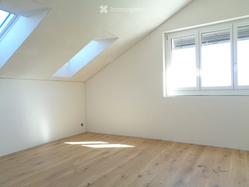 Empty room with wooden flooring, white walls, and large windows, including skylights, with no furniture or equipment.