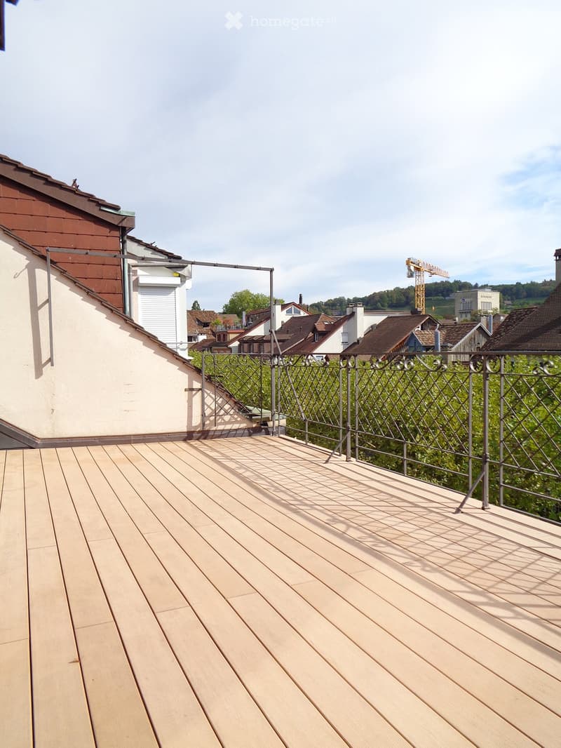 Wooden deck with metal railing, overlooking a residential area with houses and greenery.