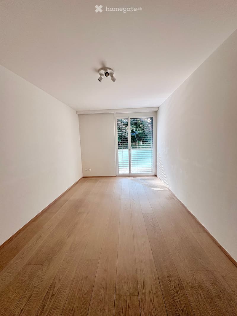 Empty room with light wooden flooring, white walls, and a large sliding glass door leading outside.