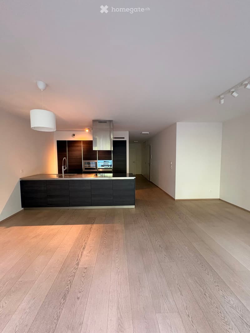 Empty kitchen area with wooden flooring, dark cabinetry, and a stainless steel range hood. No furniture or appliances are present.