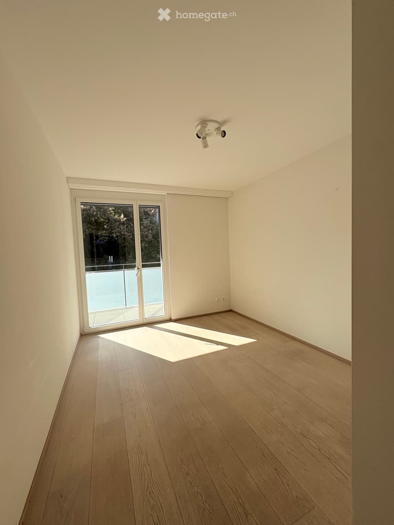 Empty room with light wooden flooring, white walls, and a large sliding glass door leading to a balcony.