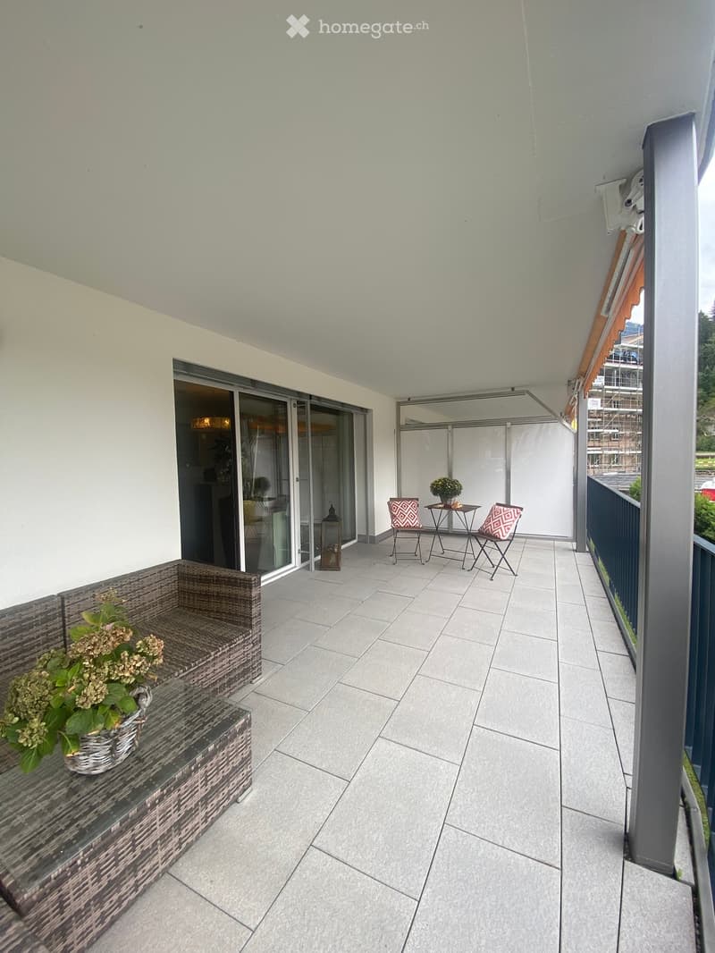 Balcony with tiled floor, wicker sofa, small table, chairs, flower pot, and lantern.