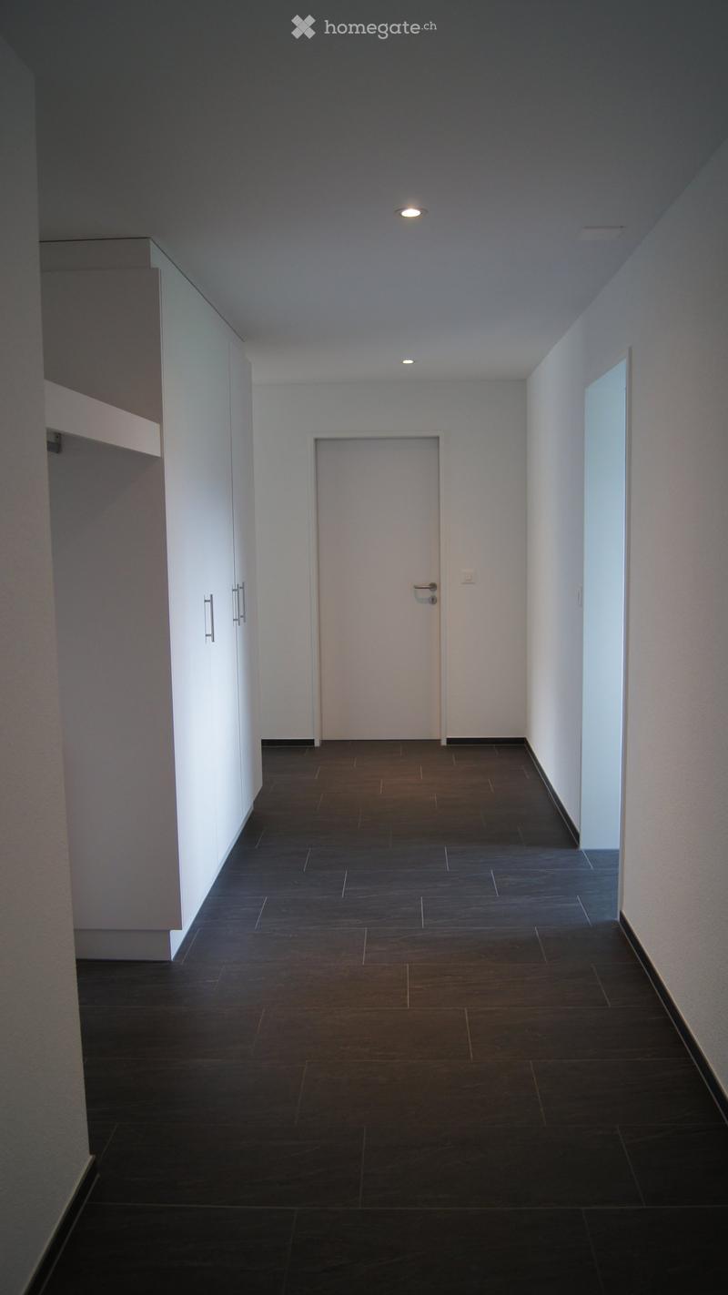 Empty hallway with dark tiled floor, white walls, and a closed door at the end.