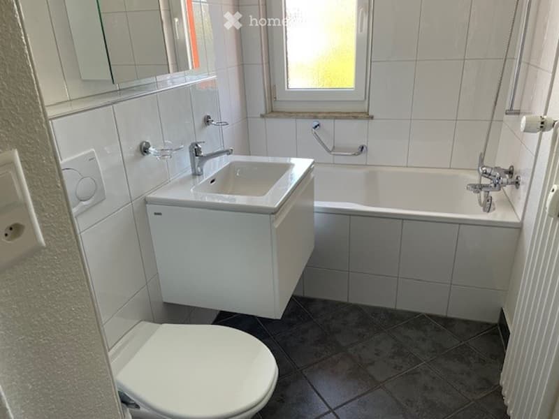 Modern bathroom with white tiles, a sink with a faucet, a bathtub, a toilet, and a mirror above the sink.