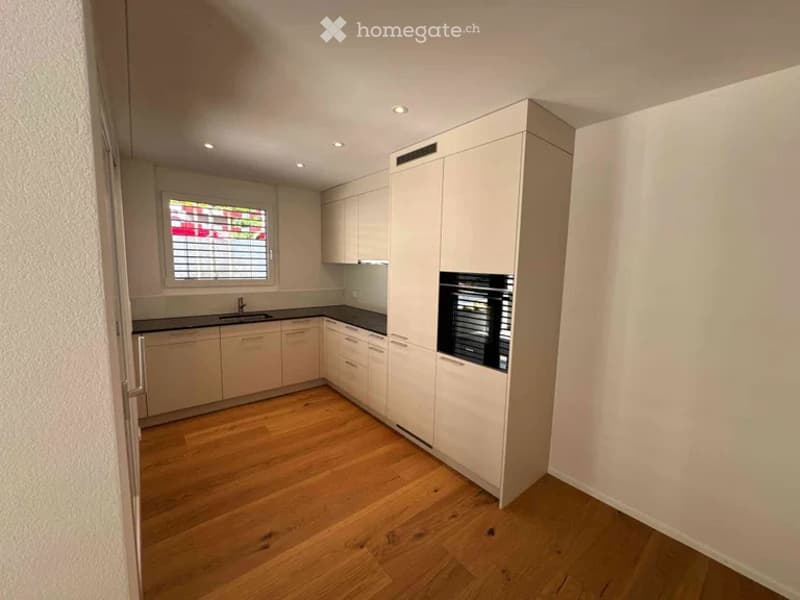 Modern kitchen with light-colored cabinets, a window with blinds, and a wooden floor.